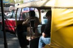 John sits in traffic, in autorickshaw. Can you see Pam in the mirror?