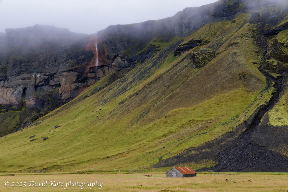 Scenery along the Ring Road, showing a barn, a steep cliffside, and a waterfall on the cliff.