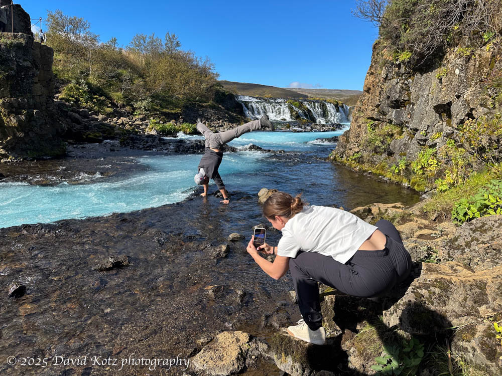photo of a man doing handstand in the Brúará river, close to Brúarárfoss waterfall, while his female partner photographs him.