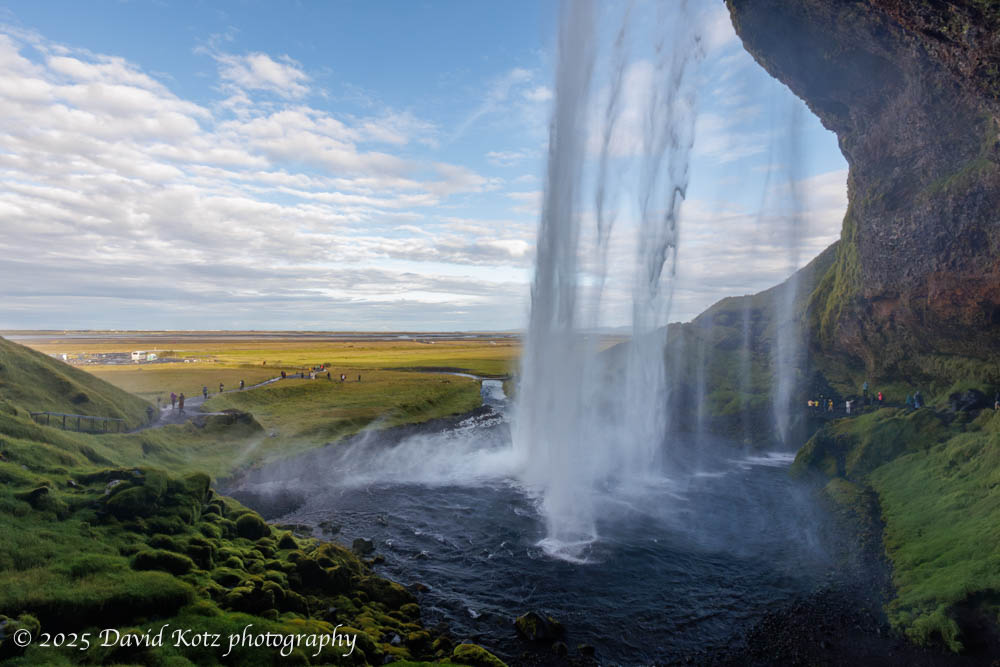 photo of Seljalandsfoss, from behind, with tiny people visible at the base of the falls.