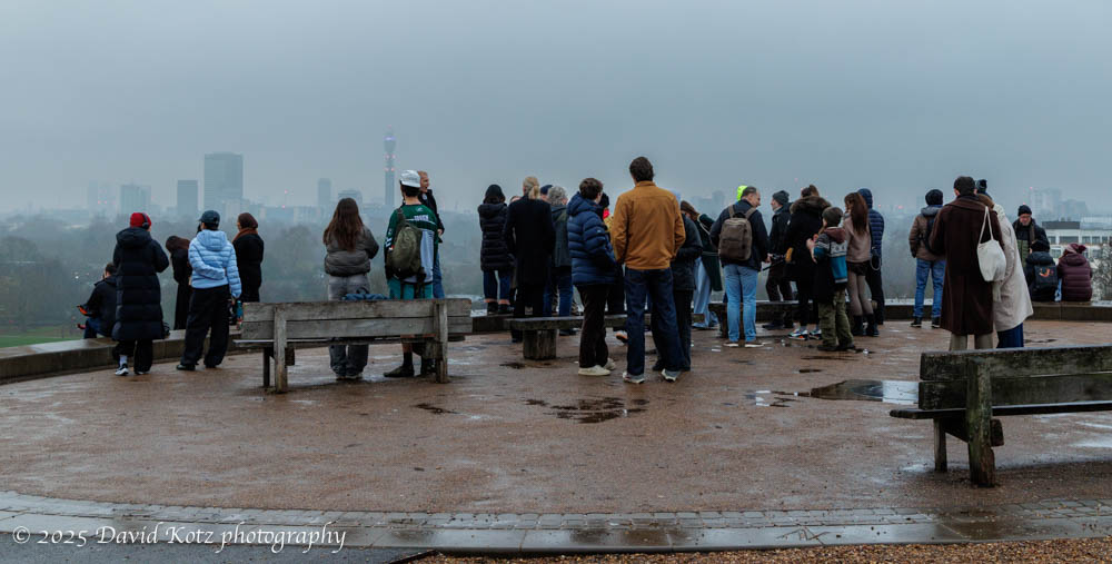 a group of people on a stone plaza, with London skyline visible in a misty gray background