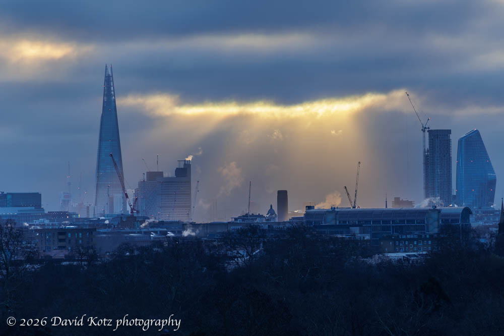 the sun is behind clouds but "god rays" shine down from the clouds onto the cityscape.