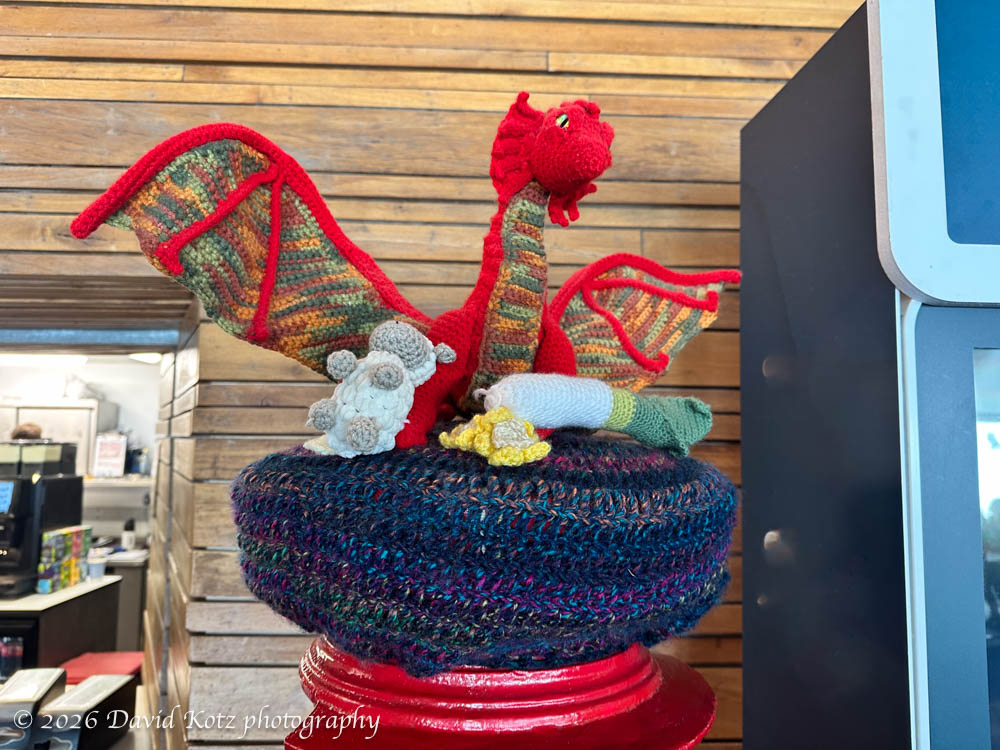 crocheted dragon with sheep, on top of the postbox.